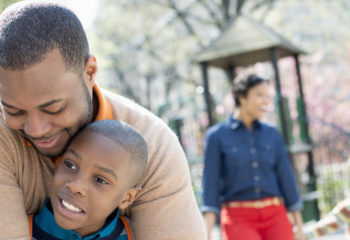 A New York city park in the spring. A family, parents and two boys spending time together. A father hugging his son.