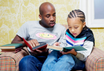 father and son reading books on chair